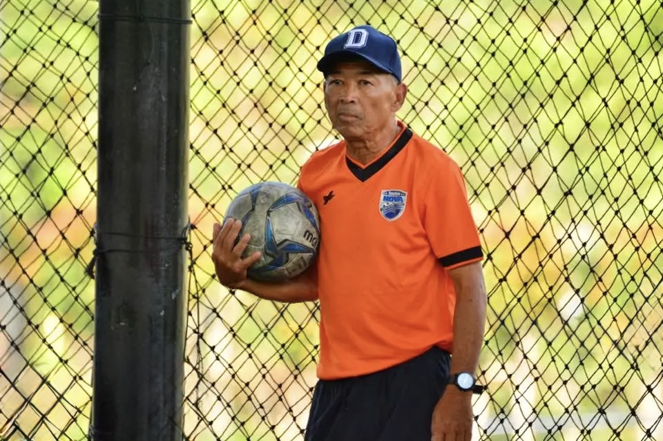 Coach Dang holding a soccer ball beside a goal
